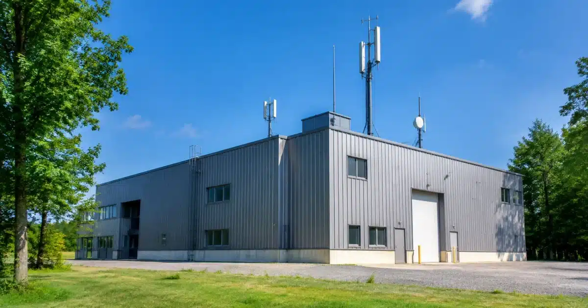 Batiment industriel gris avec antennes sur terrain plat entouré arbres