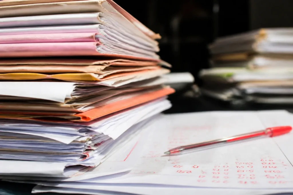 Dossiers administratifs empiles chiffres manuscrits stylo rouge